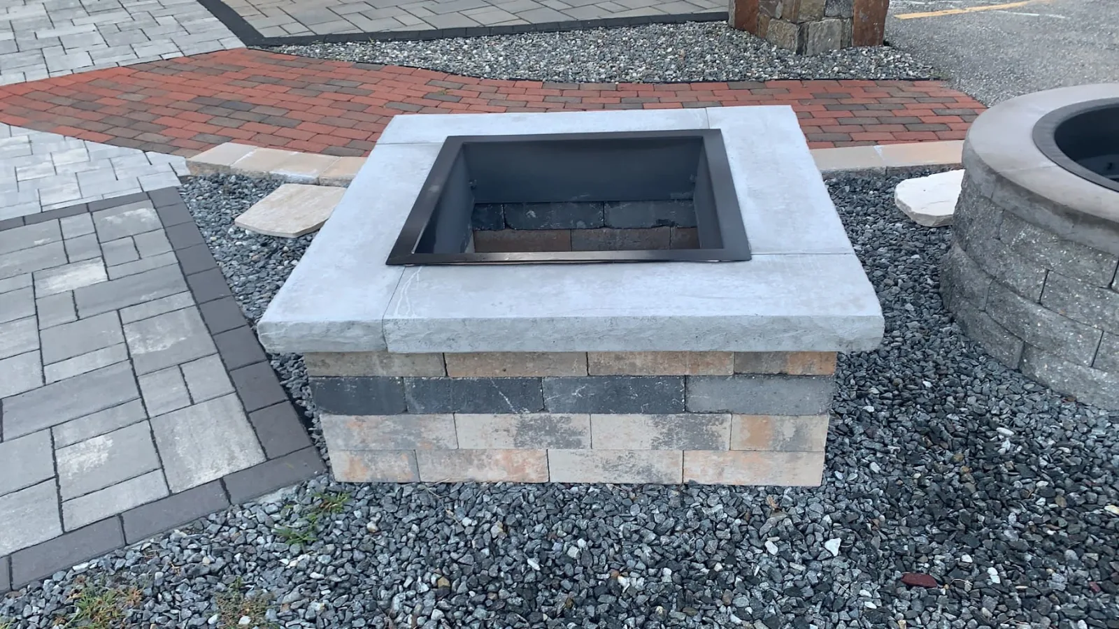 Square fire pit with a granite cap and stone veneer surround set into a paver patio