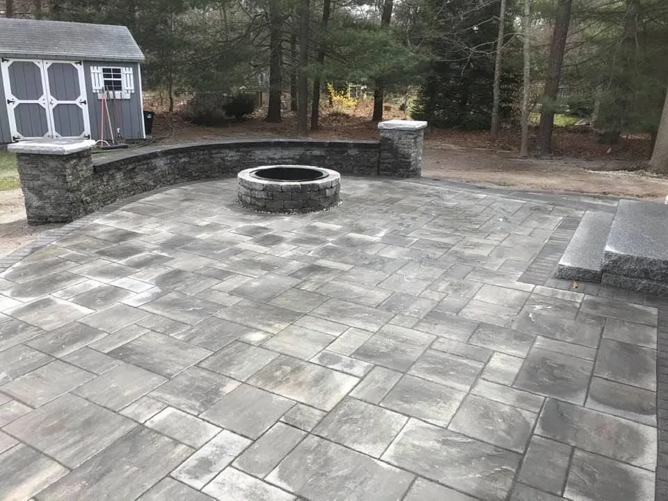 Large paver patio with a round fire pit and a capped stone seat wall with pillars