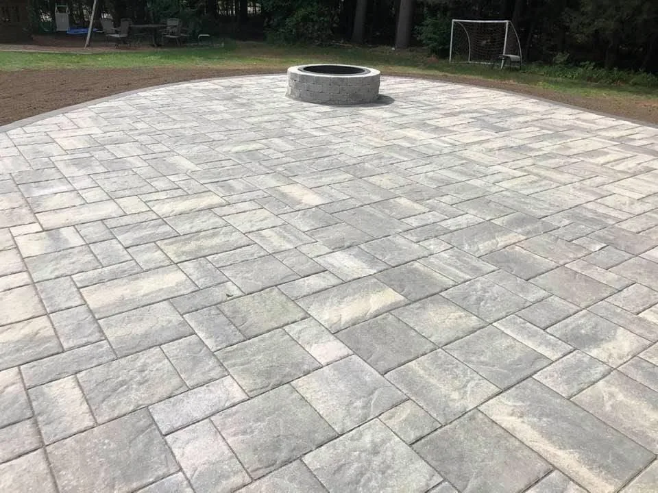 Wide paver patio laid in a random pattern with a round fire pit at the far end