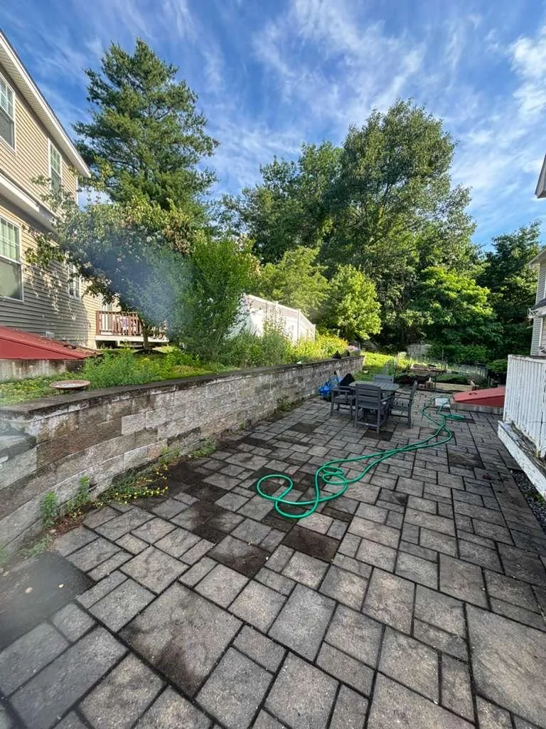 Paver patio in a backyard with outdoor furniture and a stone retaining wall behind it