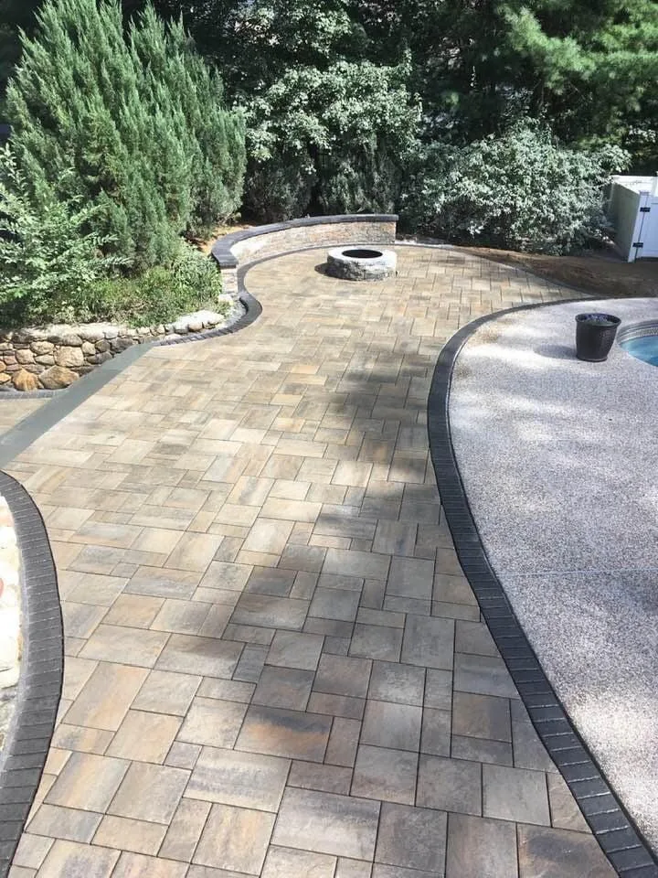 Curved paver patio with a fire pit running alongside a pool surround