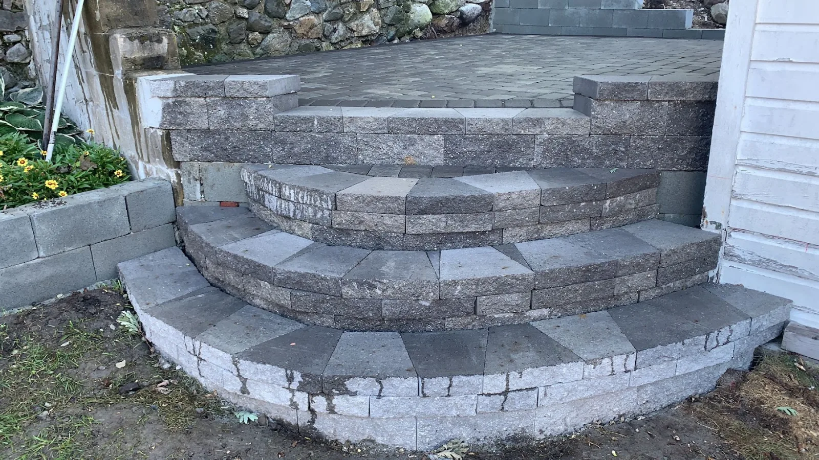 Curved granite and block steps rising into a raised paver patio