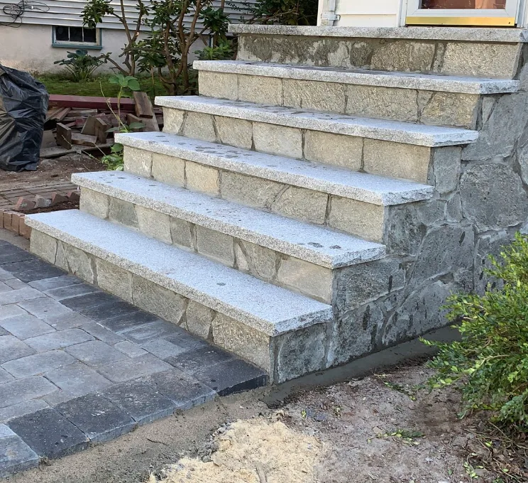 Granite steps with fieldstone risers and a brick paver border alongside a planting bed