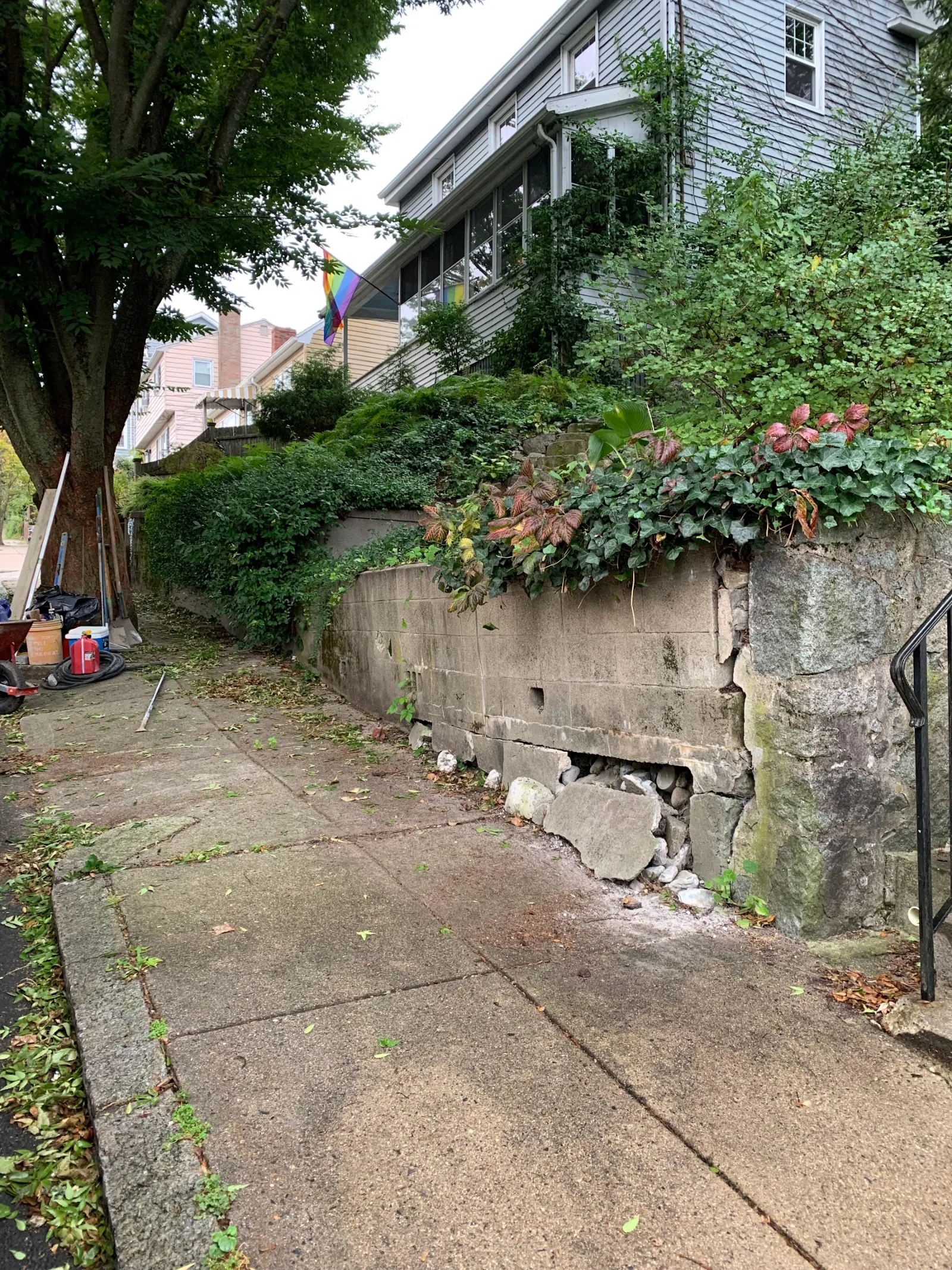 A failing old stone and concrete wall bulging and losing material, before replacement
