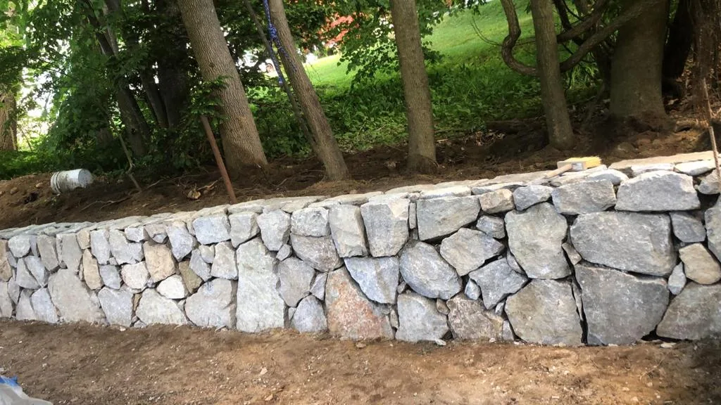 Natural fieldstone retaining wall holding back a wooded slope